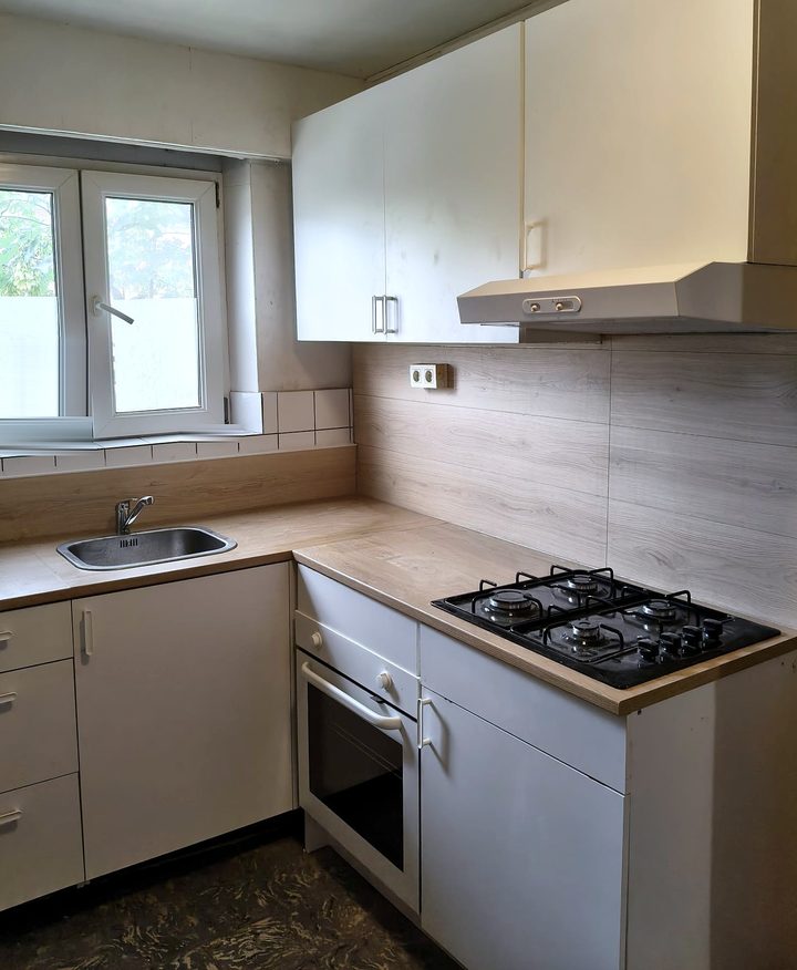 Gerenoveerde keuken met lichtgrijze kasten, donker werkblad en betegelde achterwand